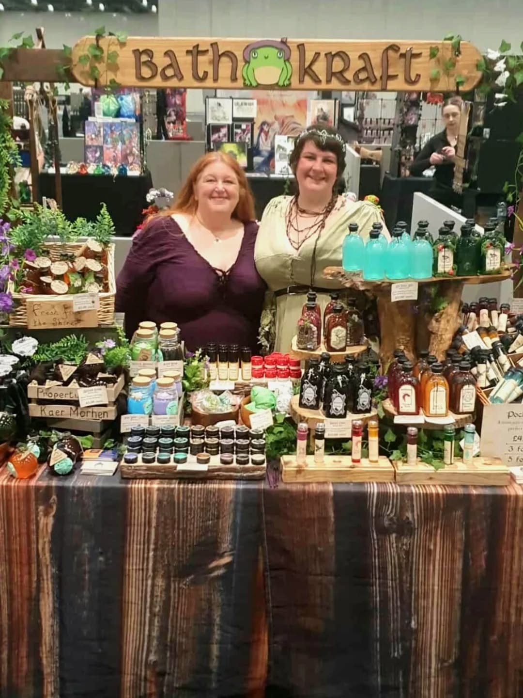 Two women standing behind a table with various products at a Bath & Body Works event.